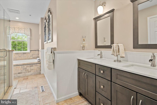 full bath with a stall shower, a bath, double vanity, stone tile flooring, and wainscoting