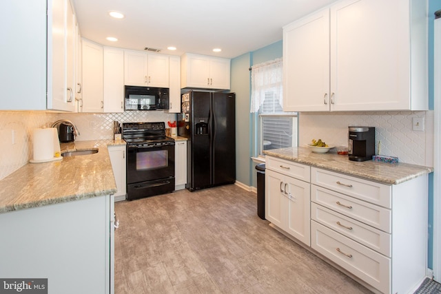 kitchen featuring black appliances, a sink, decorative backsplash, white cabinets, and light stone counters