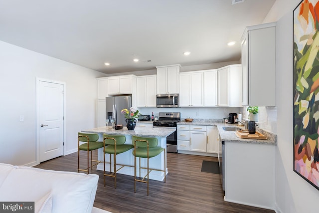 kitchen with dark wood-style flooring, appliances with stainless steel finishes, a center island, white cabinetry, and a kitchen bar