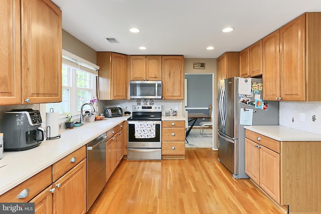 kitchen with decorative backsplash, visible vents, appliances with stainless steel finishes, a sink, and light wood finished floors