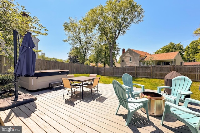wooden terrace with outdoor dining area, a lawn, a hot tub, a fenced backyard, and a fire pit