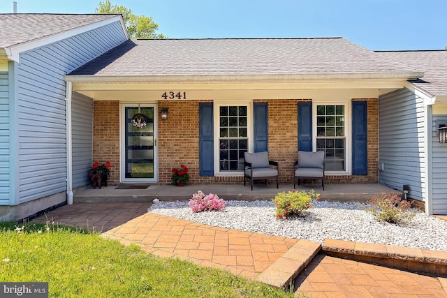 view of exterior entry featuring brick siding, roof with shingles, and covered porch