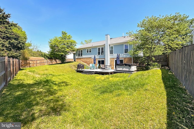 rear view of property featuring a deck, a fenced backyard, brick siding, a hot tub, and a yard