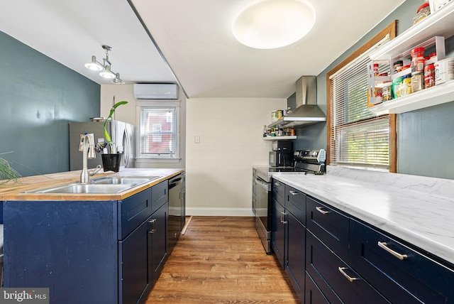kitchen featuring wall chimney range hood, light countertops, a wall unit AC, light wood-style flooring, and stainless steel appliances