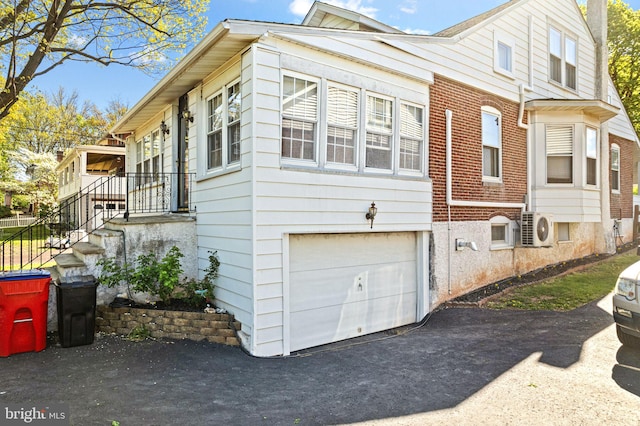 view of side of property with brick siding, an attached garage, driveway, and ac unit