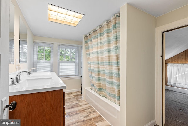 full bathroom with double vanity, wood finished floors, a sink, baseboards, and shower / bathtub combination with curtain