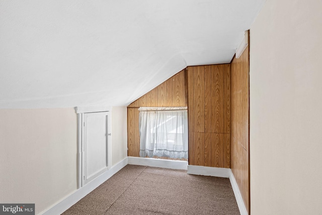 additional living space with baseboards, wood walls, carpet, and lofted ceiling