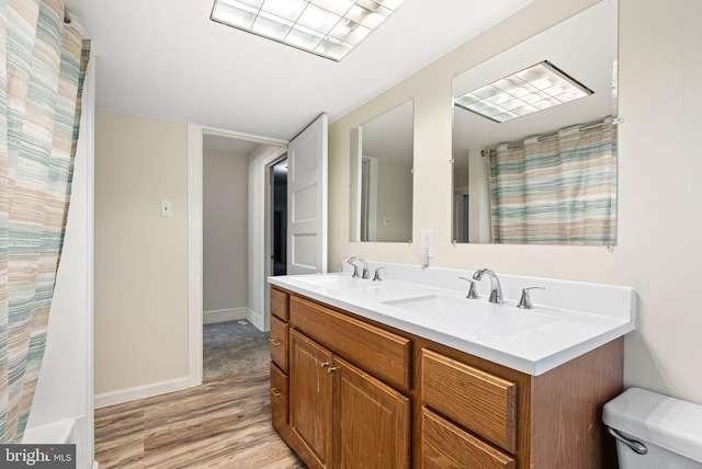 full bath featuring double vanity, a sink, wood finished floors, and toilet
