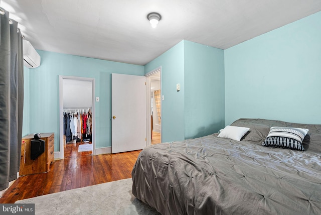 bedroom with wood-type flooring, a closet, a wall unit AC, and a spacious closet