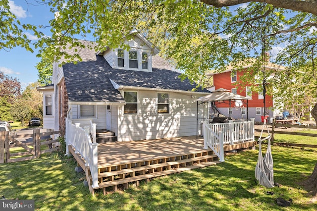rear view of property featuring fence, roof with shingles, a gazebo, a deck, and a lawn