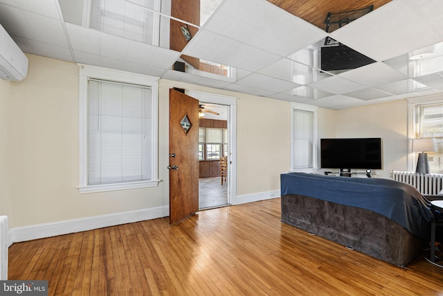 living room featuring baseboards, wood-type flooring, a wall mounted AC, and a drop ceiling