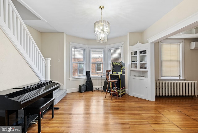 sitting room featuring an inviting chandelier, light wood finished floors, radiator heating unit, baseboards, and stairway