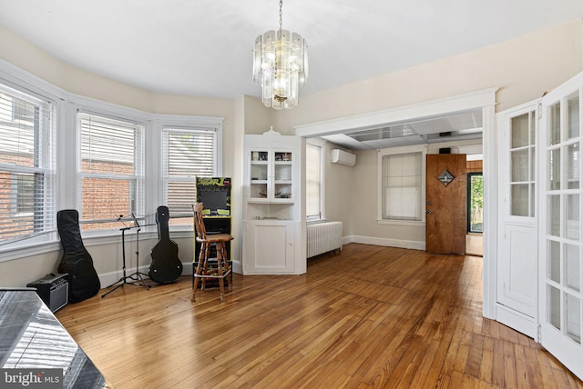 interior space featuring an AC wall unit, light wood-style flooring, radiator, and an inviting chandelier