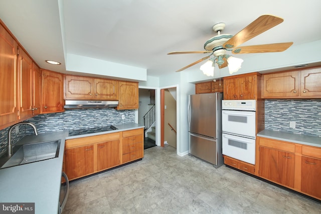 kitchen with black electric cooktop, a sink, freestanding refrigerator, double oven, and under cabinet range hood
