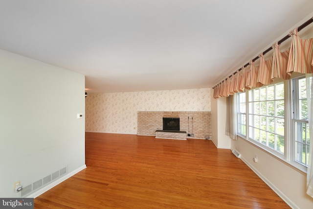 unfurnished living room with a brick fireplace, baseboards, visible vents, and light wood-type flooring