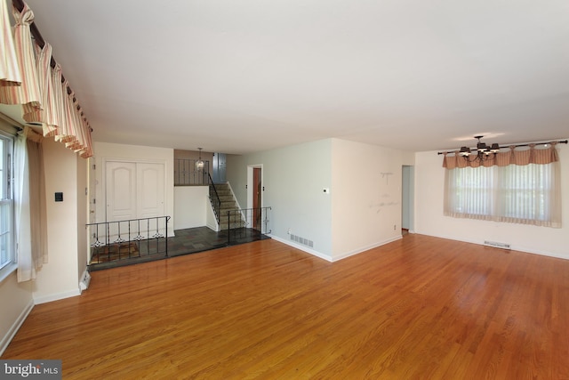 unfurnished living room with visible vents, light wood-type flooring, baseboards, a chandelier, and stairs