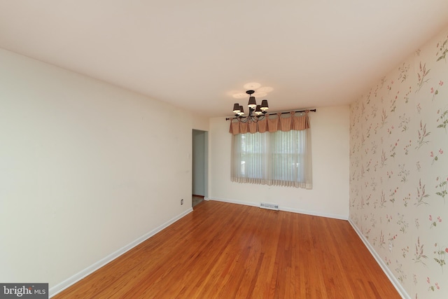 unfurnished room featuring baseboards, an inviting chandelier, visible vents, and light wood-type flooring
