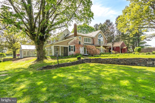 view of front of house featuring a sunroom, brick siding, a chimney, and a front yard