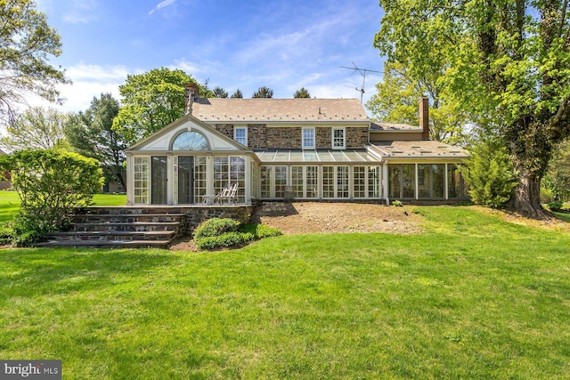 back of property featuring a sunroom, stone siding, a yard, and a chimney