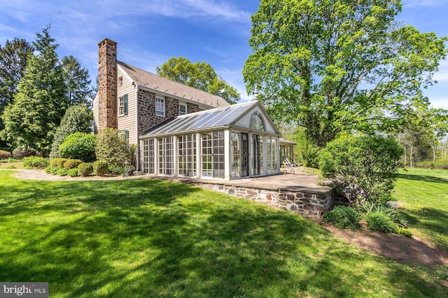 rear view of property with a sunroom, a lawn, and a chimney