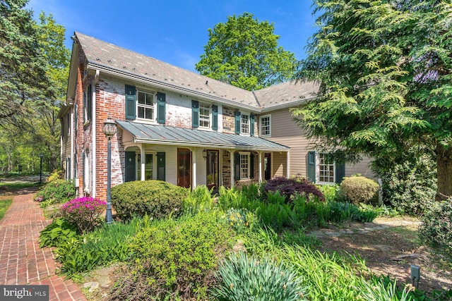 traditional-style home featuring a standing seam roof, covered porch, and brick siding