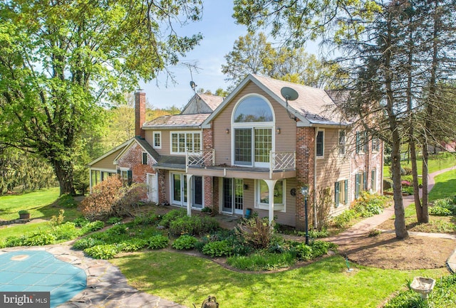 rear view of house featuring a chimney, a yard, and brick siding