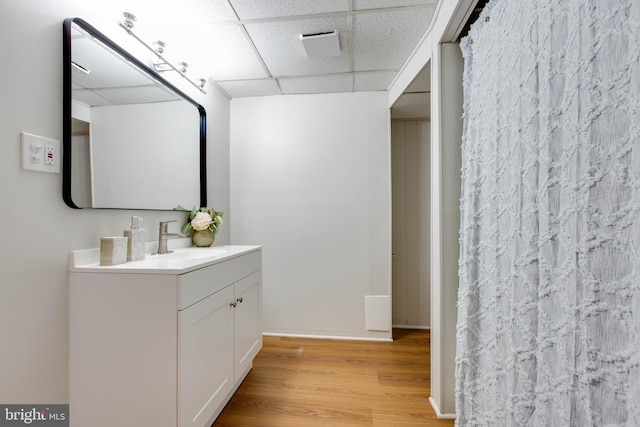 full bath with vanity, baseboards, a drop ceiling, and wood finished floors