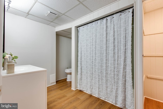 bathroom with wood finished floors, vanity, toilet, a drop ceiling, and a shower with shower curtain