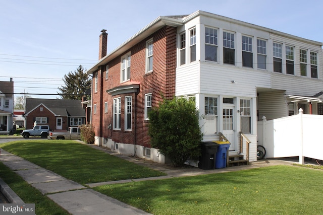 view of home's exterior with a chimney, a lawn, brick siding, fence, and entry steps