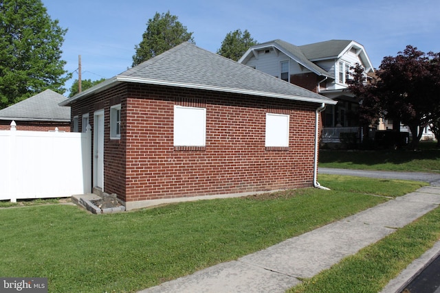view of side of home with a lawn, brick siding, fence, and a shingled roof