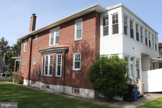 back of house with brick siding, a lawn, fence, and a chimney
