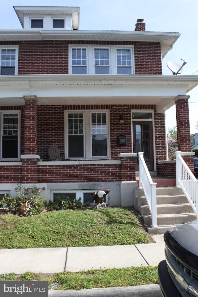 view of front of property featuring brick siding, a front yard, covered porch, and a chimney