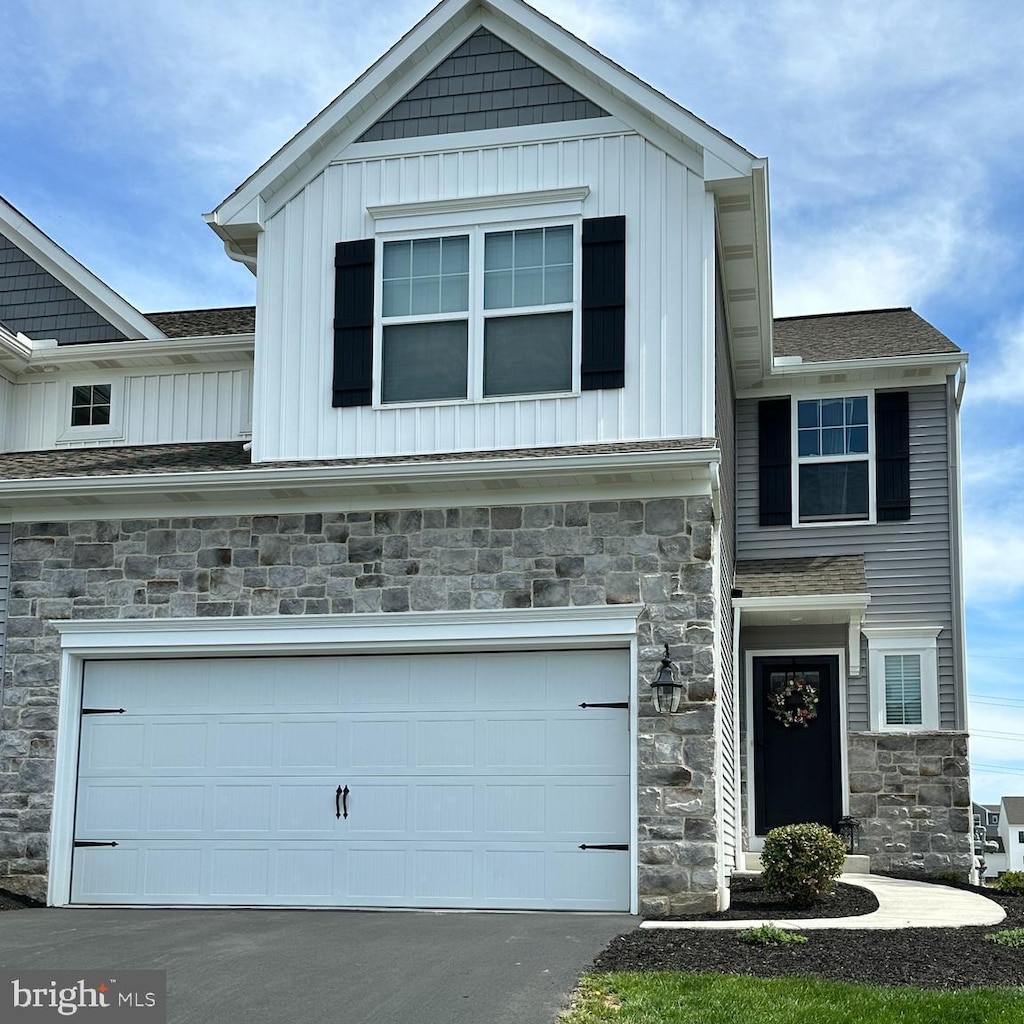 craftsman-style home featuring board and batten siding, an attached garage, stone siding, and aphalt driveway