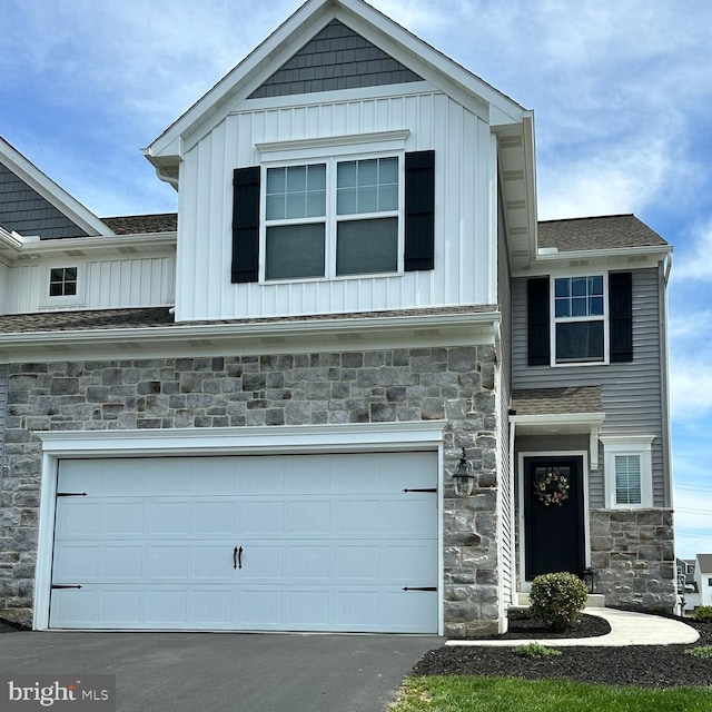 craftsman-style home featuring board and batten siding, an attached garage, stone siding, and aphalt driveway