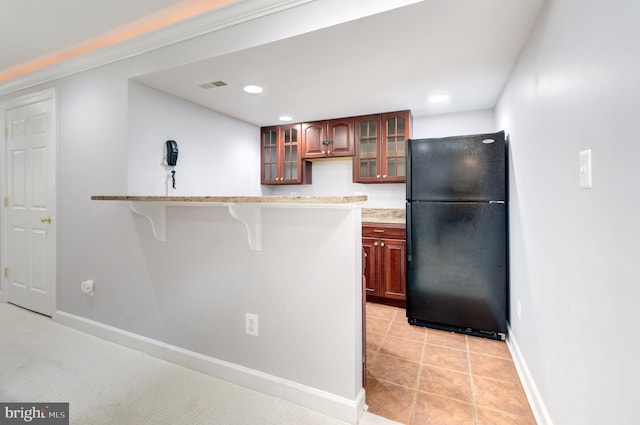 7820 Elsinore Dr, Manassas, VA 20112 - kitchen with visible vents, freestanding refrigerator, glass insert cabinets, baseboards, and a kitchen breakfast bar