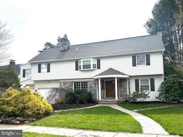 colonial house featuring a garage, stone siding, a front lawn, and a chimney