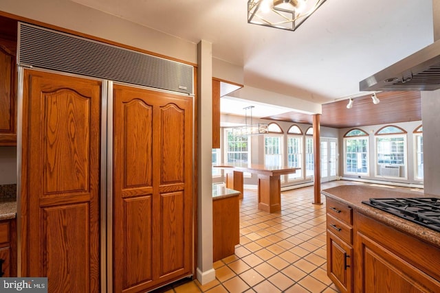 kitchen with black gas cooktop, light tile patterned flooring, brown cabinets, built in fridge, and track lighting