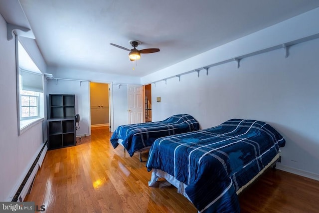 bedroom featuring a baseboard radiator, baseboards, wood finished floors, and ceiling fan