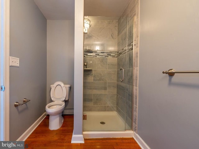 bathroom with a shower stall, toilet, baseboards, and wood finished floors