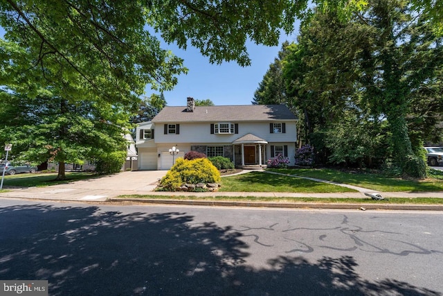 traditional-style home with an attached garage, driveway, a chimney, and a front yard