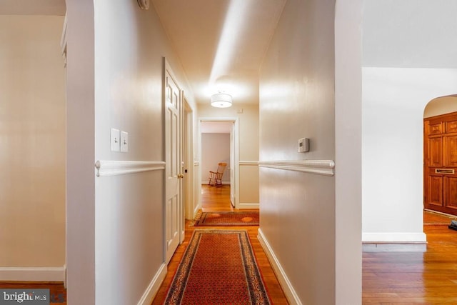 corridor with arched walkways, wood finished floors, and baseboards