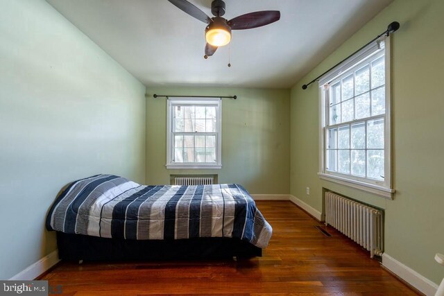 bedroom with radiator heating unit, wood finished floors, and multiple windows