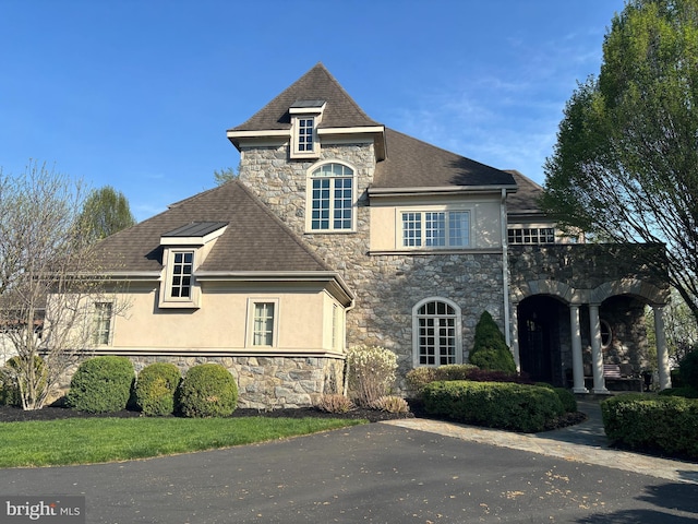 french country inspired facade with stucco siding, stone siding, and a shingled roof