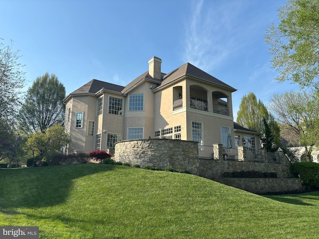 back of house with a lawn, a chimney, a balcony, and stucco siding