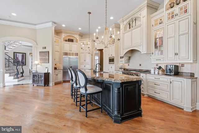 kitchen with a kitchen island with sink, light stone counters, a breakfast bar, built in appliances, and a sink