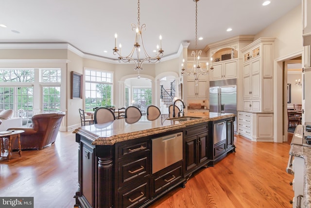 kitchen featuring an island with sink, stainless steel appliances, a notable chandelier, and a sink