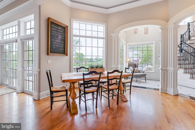 dining area with arched walkways, wood finished floors, decorative columns, ornamental molding, and stairway