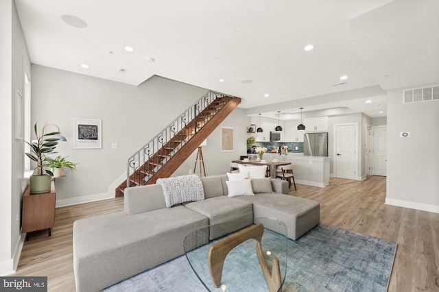 living area featuring stairway, visible vents, baseboards, and light wood finished floors