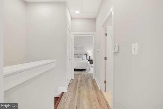 hallway featuring light wood-type flooring, recessed lighting, baseboards, and attic access