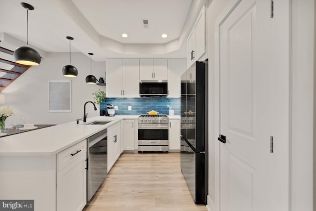 kitchen featuring hanging light fixtures, tasteful backsplash, a sink, stainless steel appliances, and light wood-style flooring